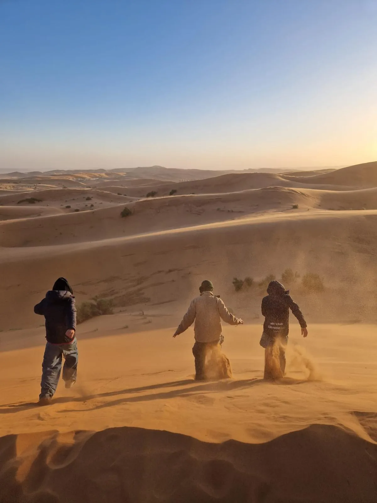 Viajeros corriendo por una duna al atardecer levantando arena