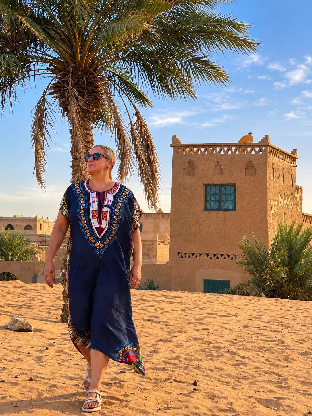 Elsa caminando bajo una palmera junto a una kasbah tradicional de adobe
