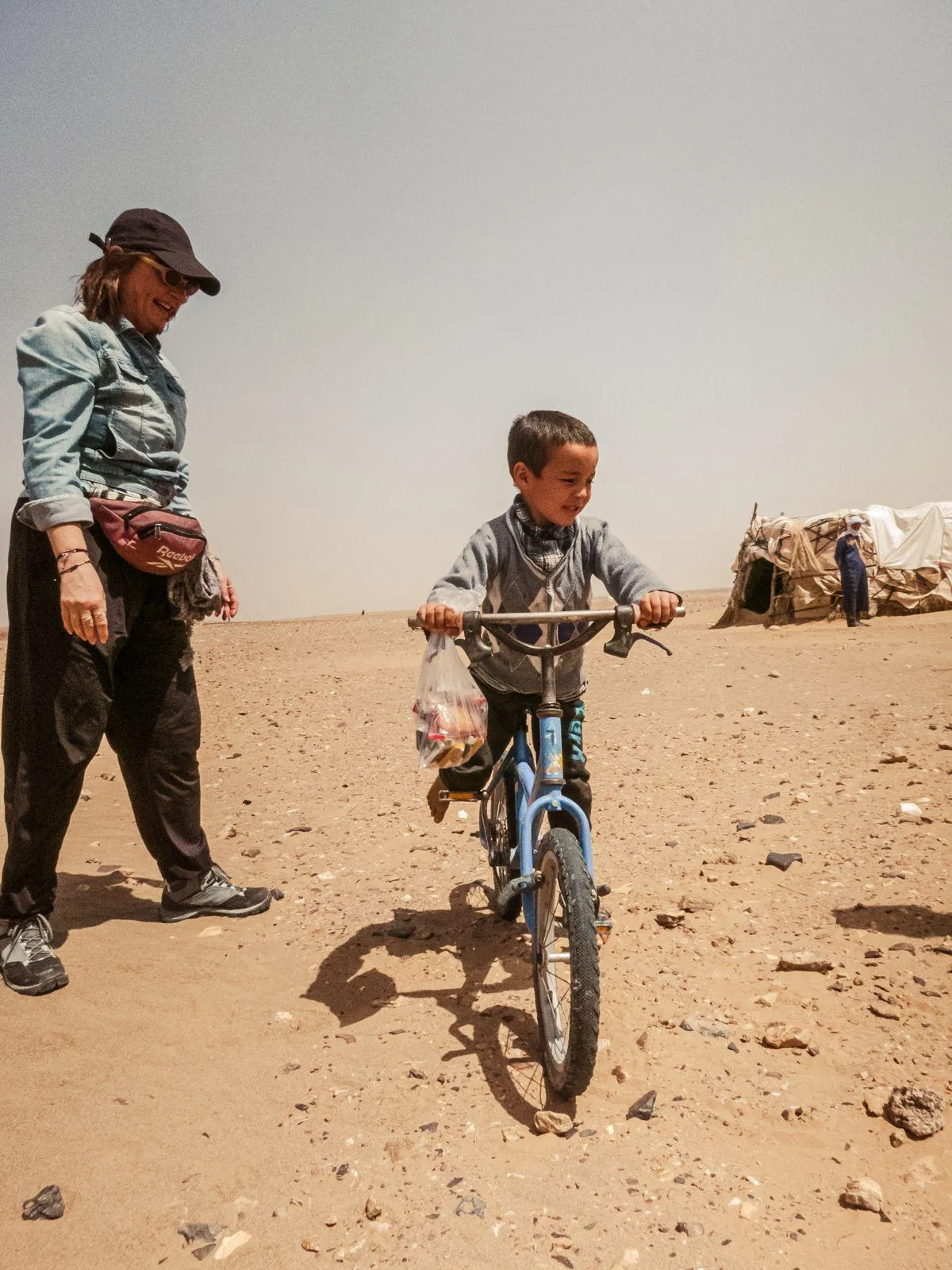 Niño nómada en bicicleta junto a una viajera en el desierto