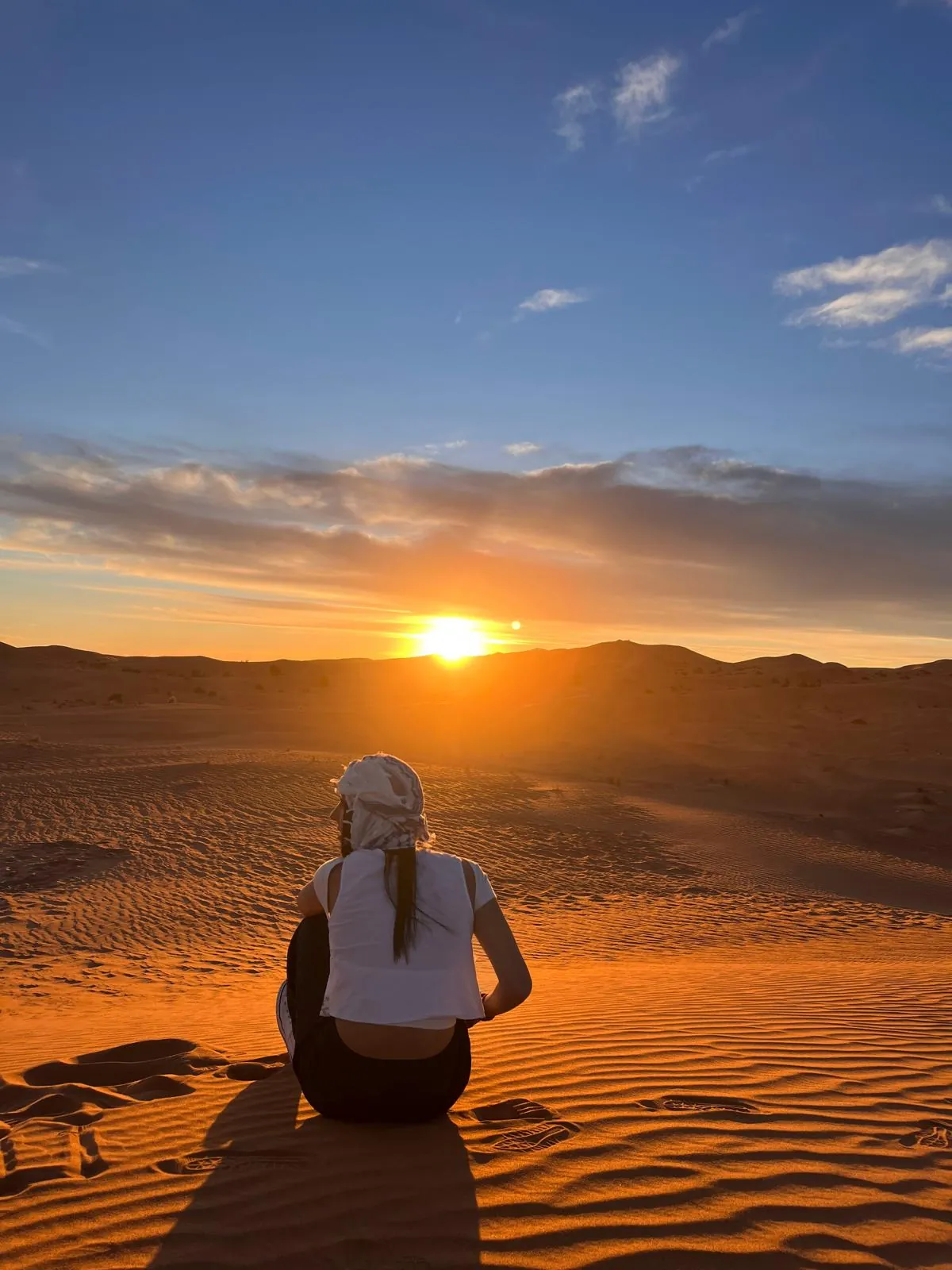 Una viajera sentada en una duna contemplando el amanecer sobre el desierto