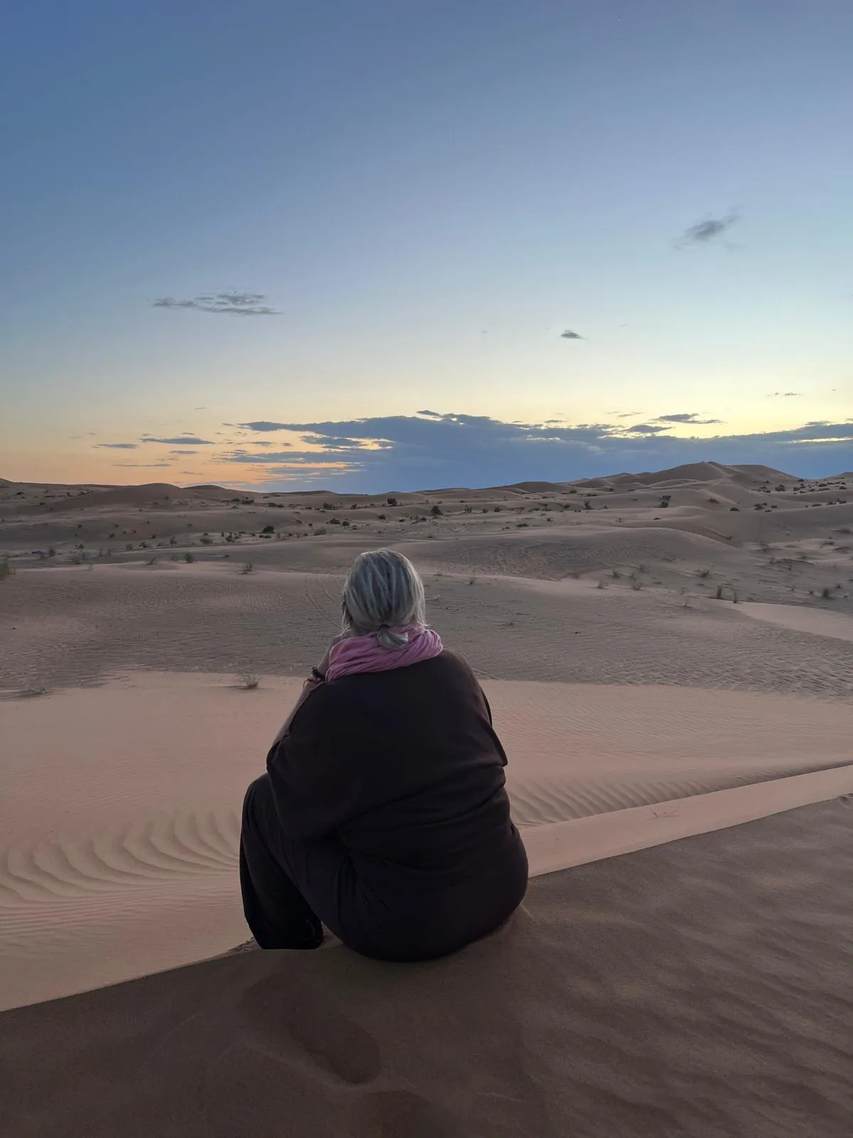 Viajera sentada en solitario sobre una duna al atardecer